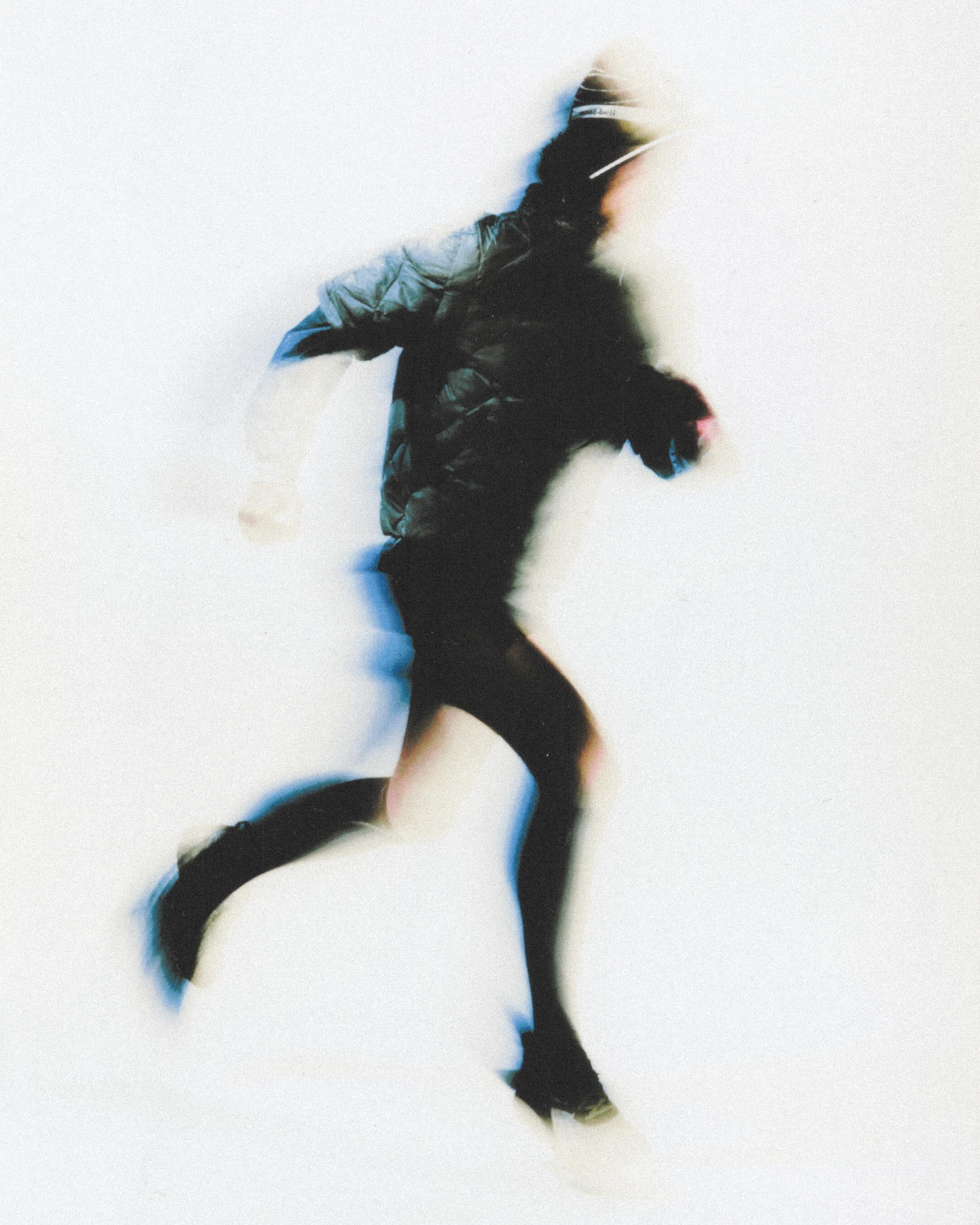 Motion-blurred figure mid-stride against a pale ground — editorial sport image.